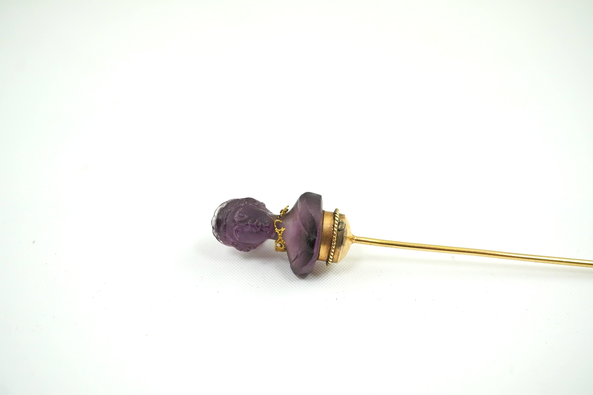 A 19th century French? gold and amethyst set stick pin, the stone carved as the bust of a lady, wearing a necklace